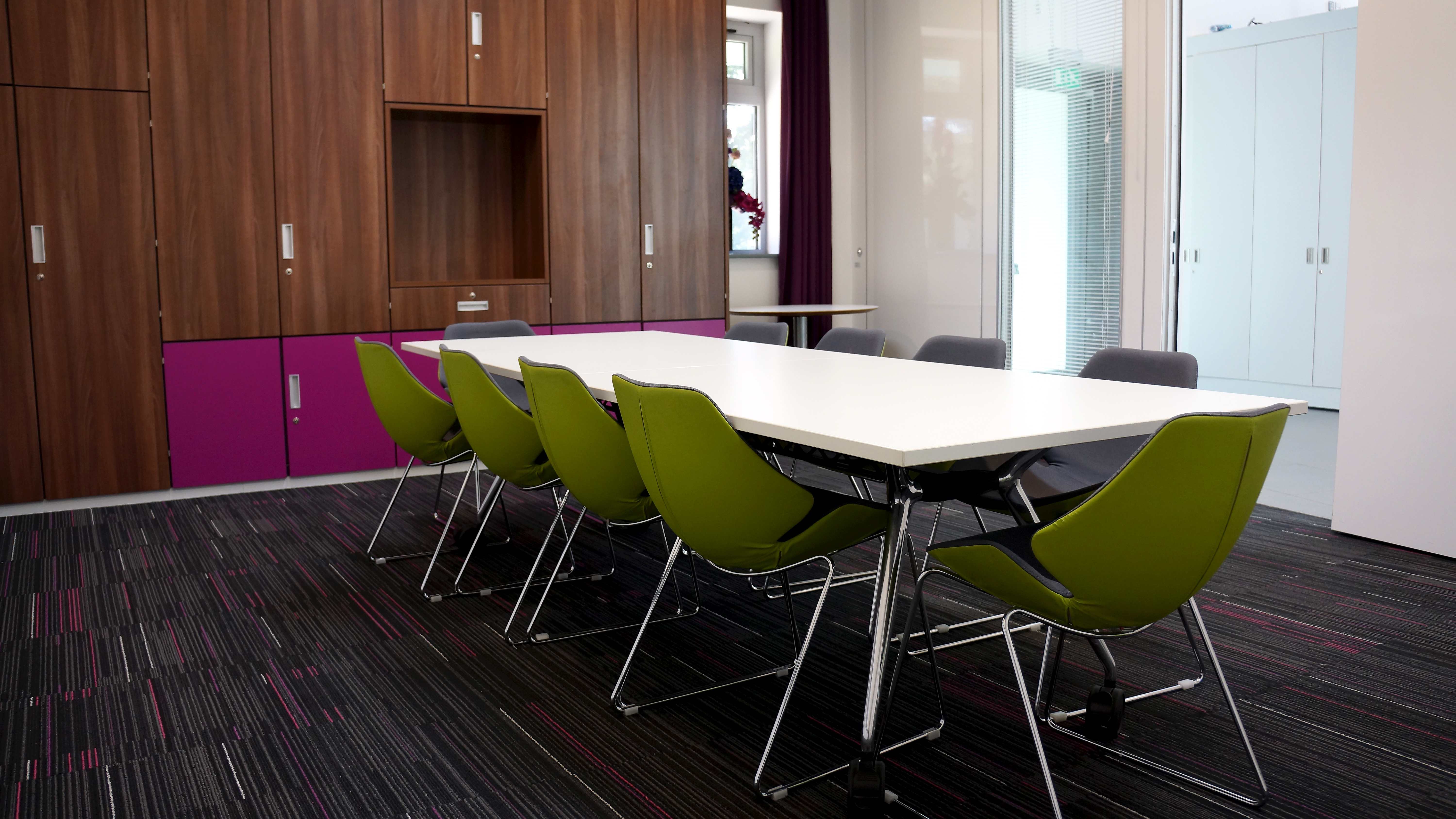 Modern boardroom with white table and green chairs, perfect for meetings and collaboration.