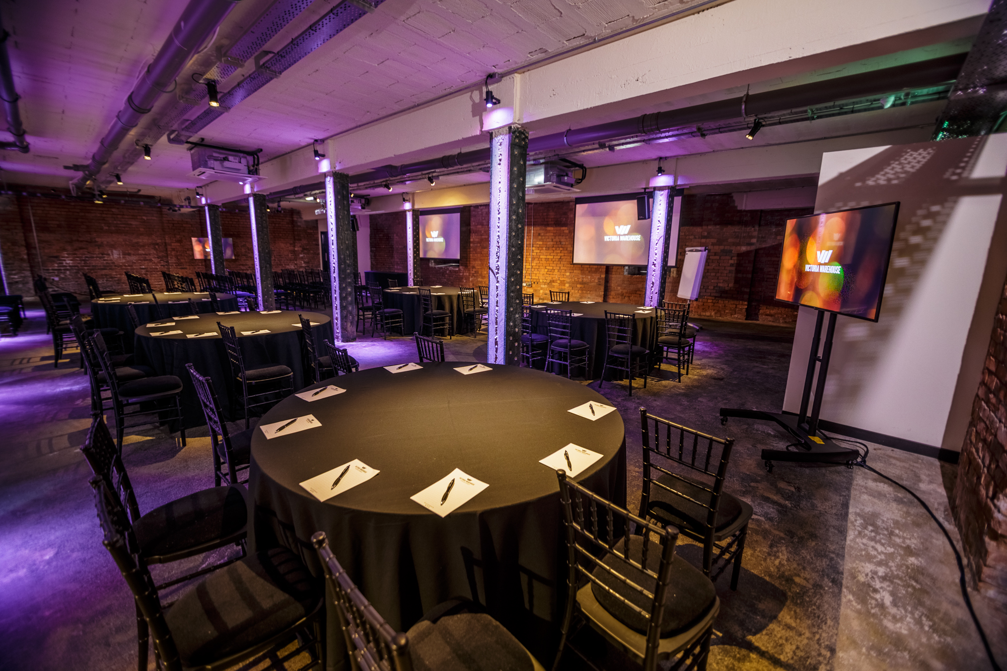 Versatile event space in Victoria Warehouse with round tables for meetings and presentations.