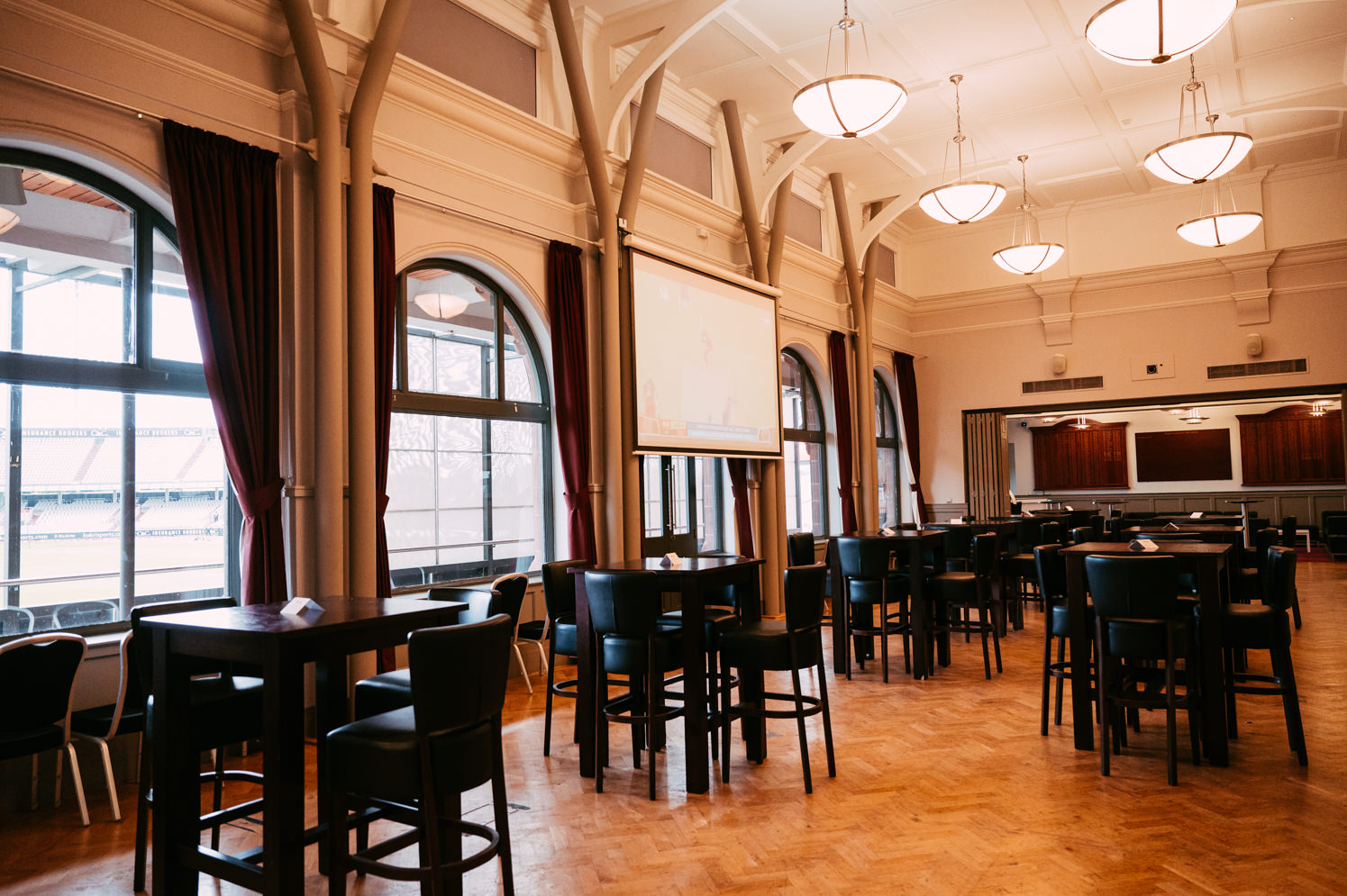 Spacious Emirates Old Trafford Members Suite for corporate events with tall tables and projector.