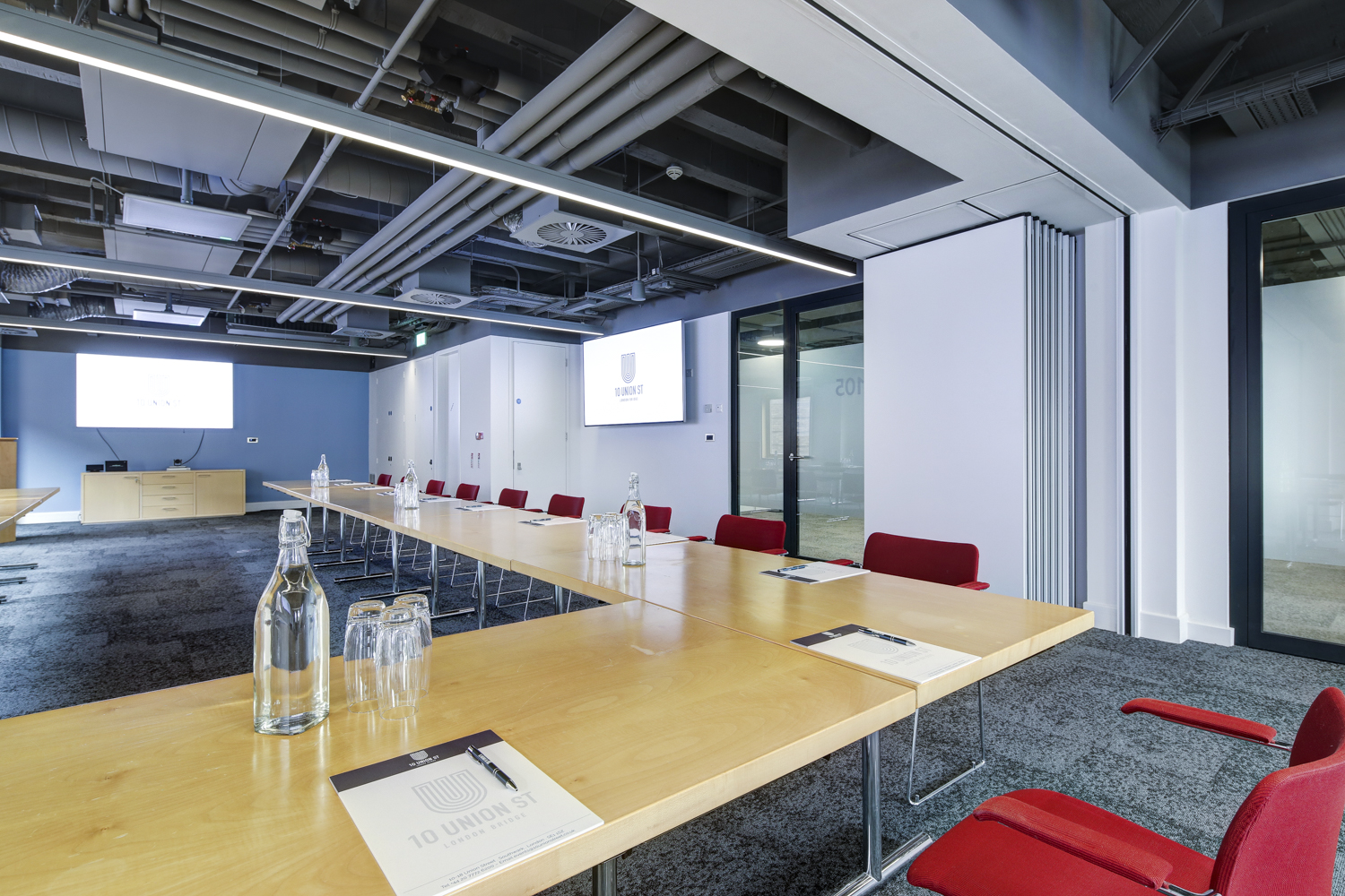 Modern meeting room with wooden table and red chairs, perfect for corporate workshops. - Banner