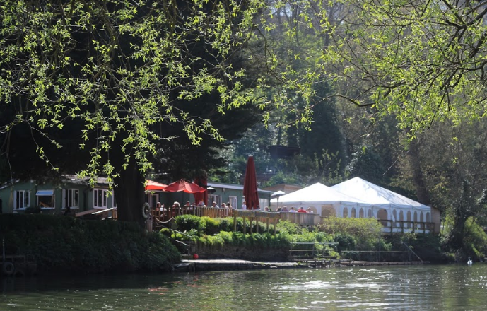 Lakeside outdoor venue with white tent and red umbrellas for events and meetings. - Banner