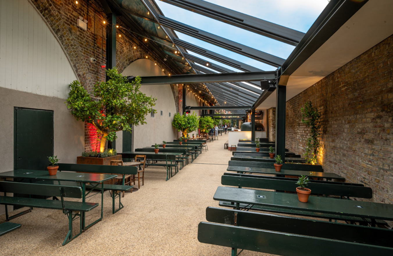 Spacious event space with communal tables and greenery, perfect for gatherings and workshops. - Banner