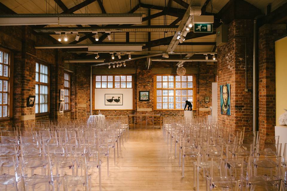 Versatile event space with acrylic chairs, exposed brick walls, ideal for meetings and gatherings. - Banner