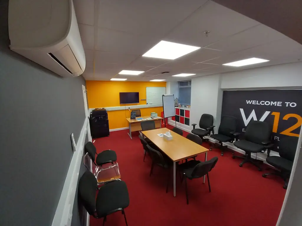 Conference room with central table, bright orange wall, ideal for meetings and events. - Banner
