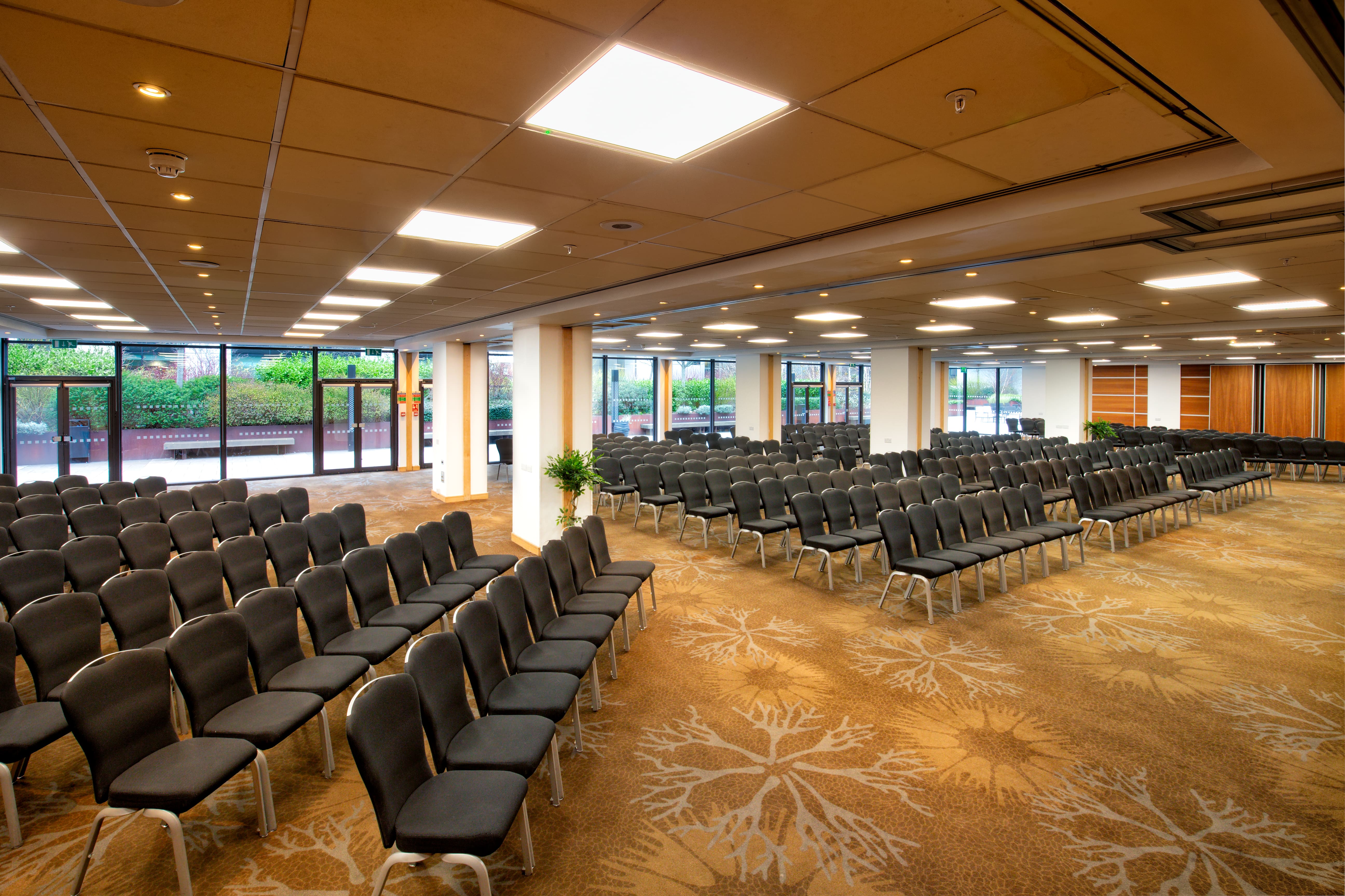 Spacious conference room at Novotel London West with black chairs and greenery view.