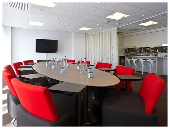 Modern conference room with oval table and red chairs at Novotel London West.