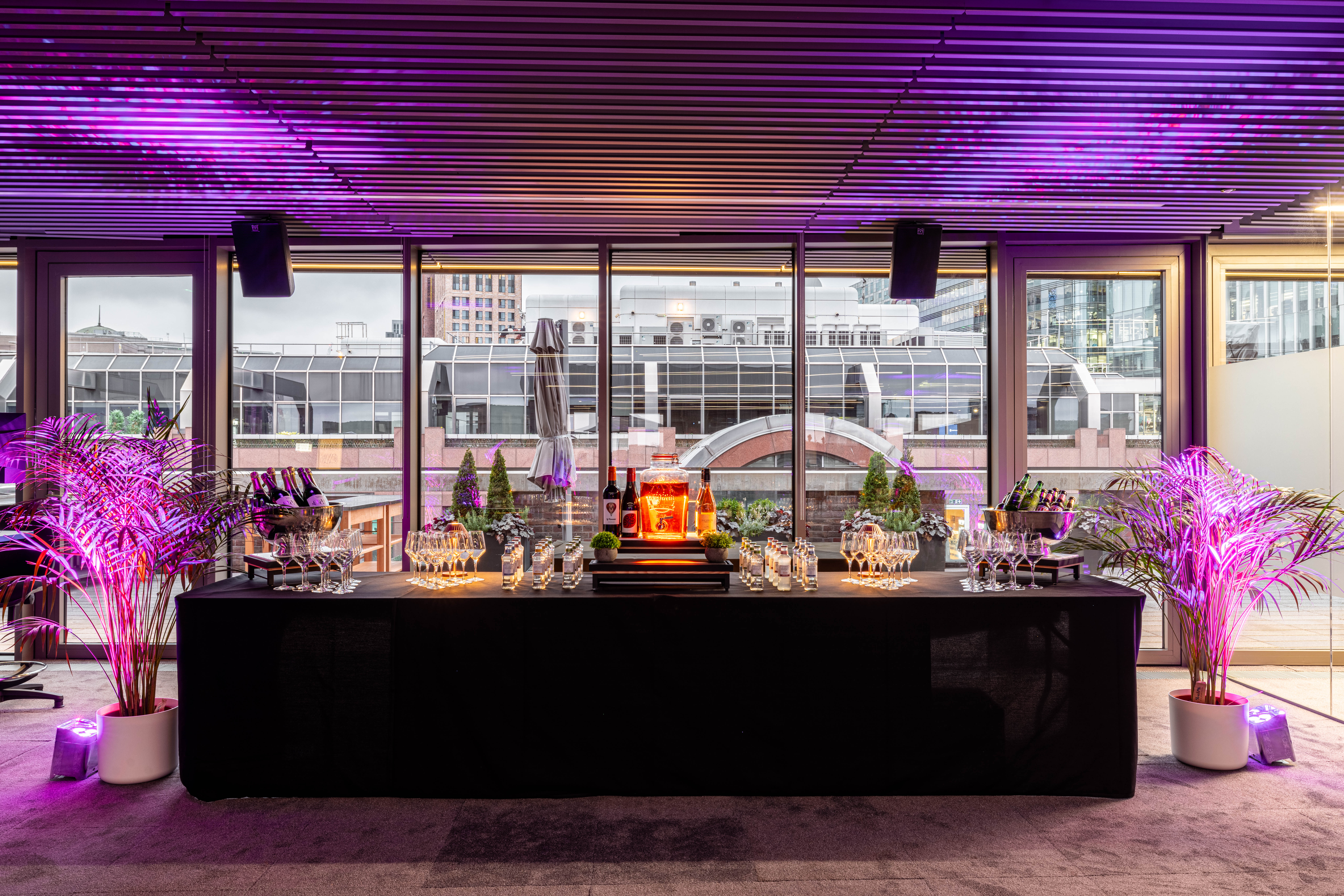Summer party rooftop with sleek black bar, champagne, and vibrant purple lighting.