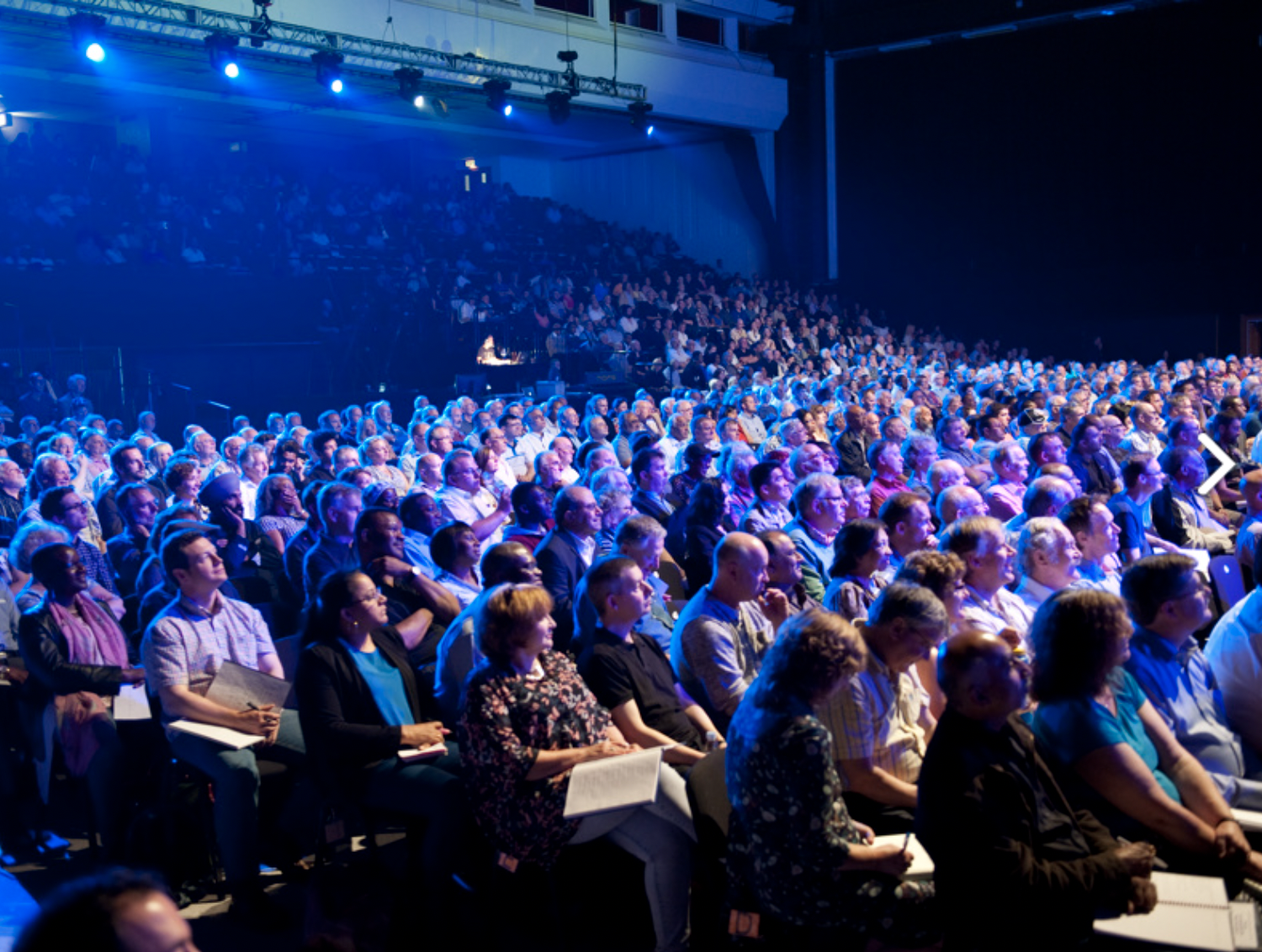 Packed auditorium at Brighton Centre with vibrant stage lighting for engaging events. - Banner
