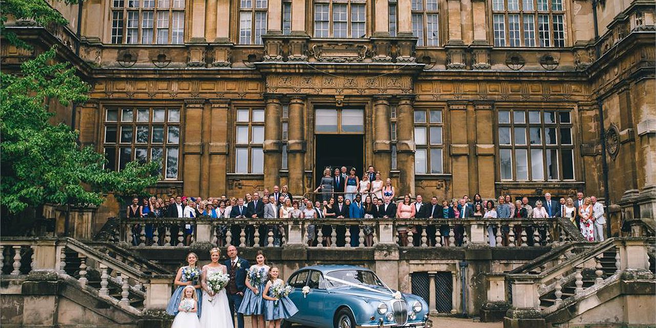 Elegant outdoor wedding at Wollaton Hall with vintage car and scenic deer park backdrop.