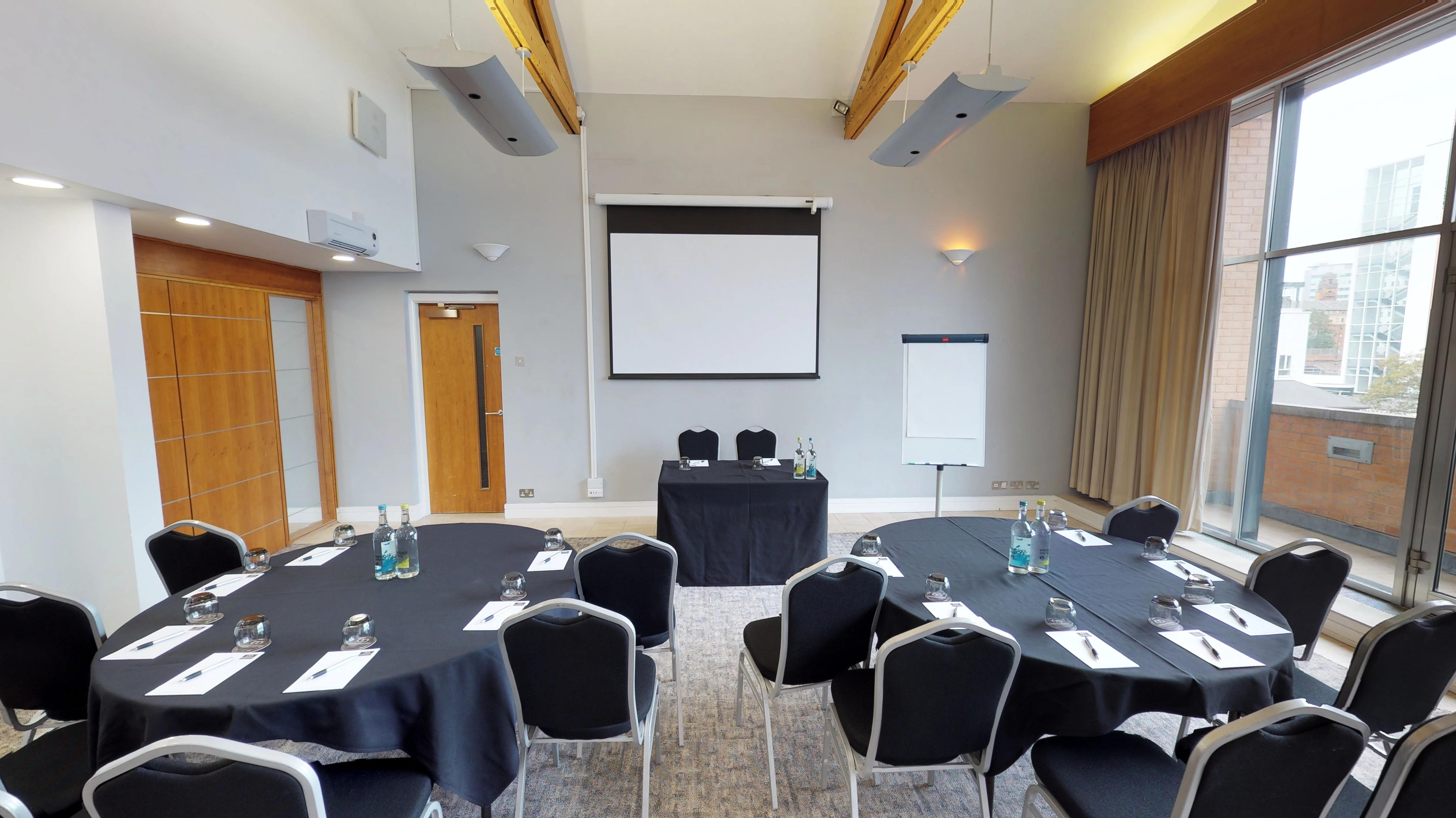 Meeting room with round tables and screen at Manchester Conference Centre for workshops.